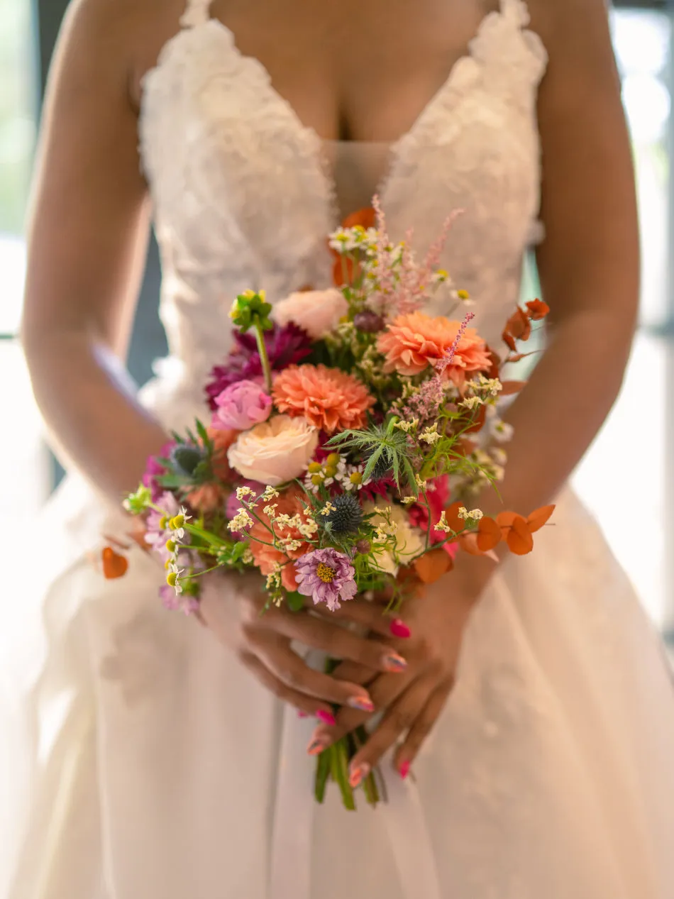 Bouquet coloré tenu devant une robe de mariée en dentelle