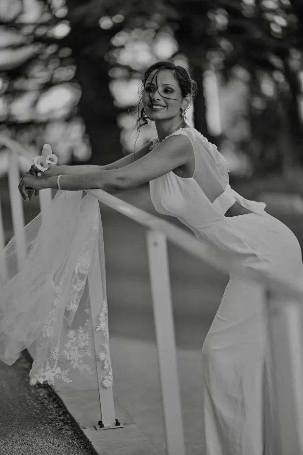 Mariée souriante accoudée à une rambarde, robe fluide, noir et blanc
