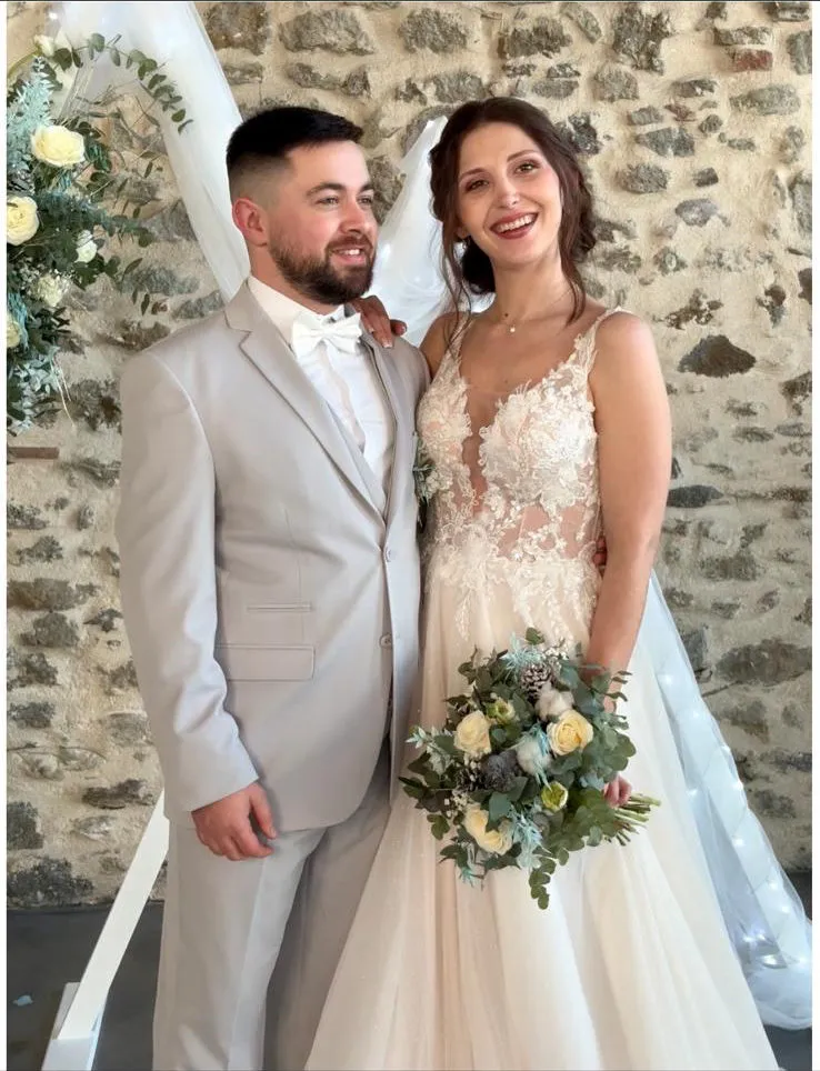 Emma et Arthur, mariés souriants devant une arche fleurie